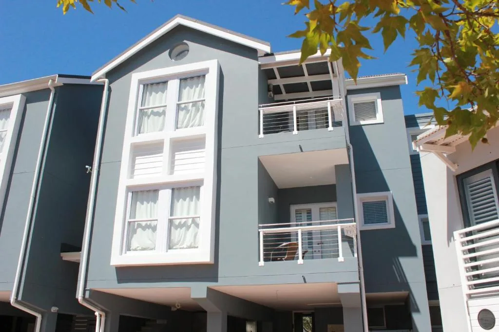 Modern three-story apartment building with gray and white facade, balconies, and clear blue sky