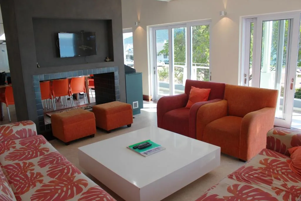 Modern lounge with orange sofas, white coffee table, and waterfront views through glass doors