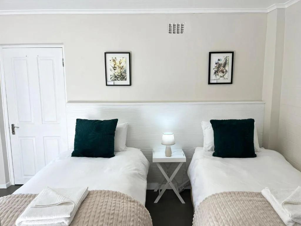 Twin bedroom with white linens, dark green cushions, and bedside table lamp