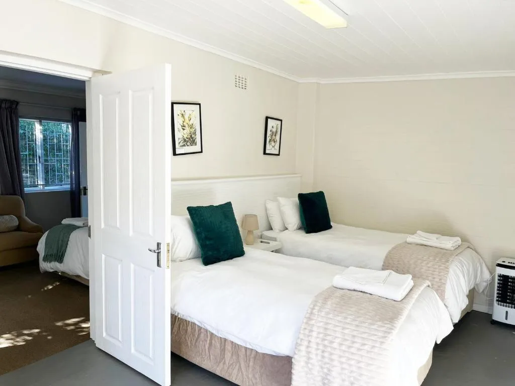Twin beds with white linens and teal cushions in bright, neutral bedroom