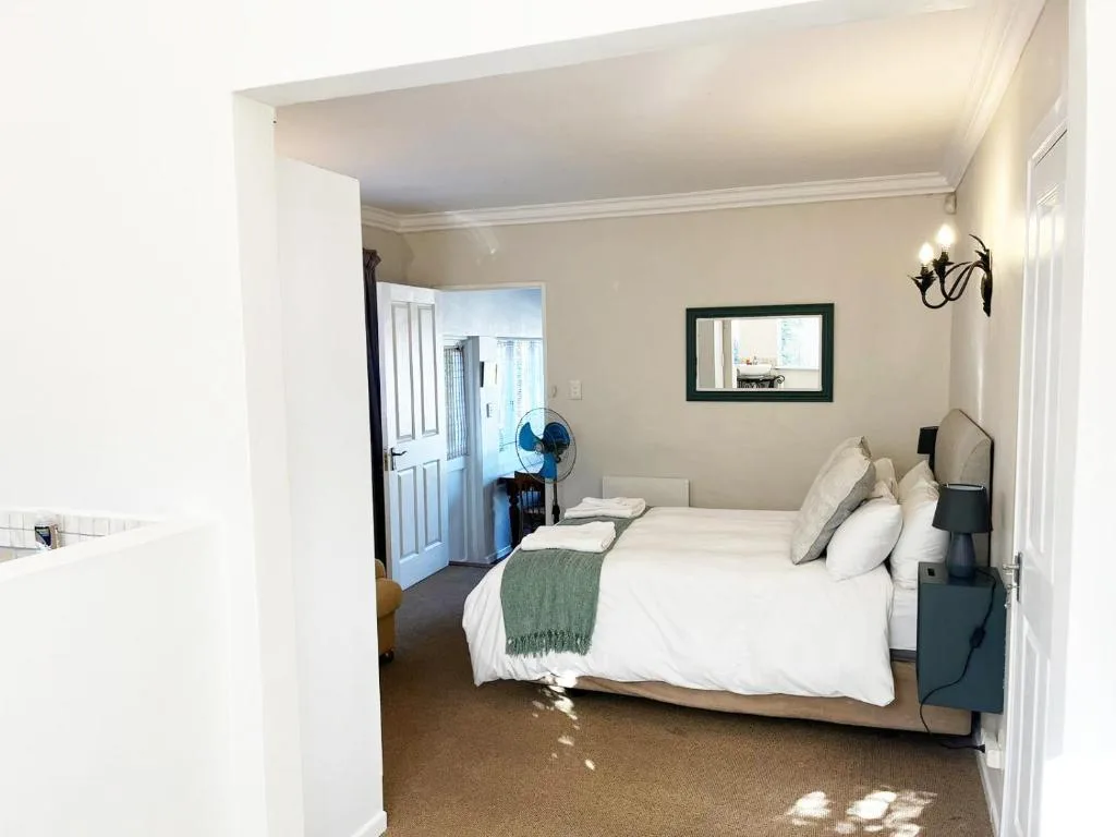 Bright bedroom with white linens, green throw, and ensuite entrance visible