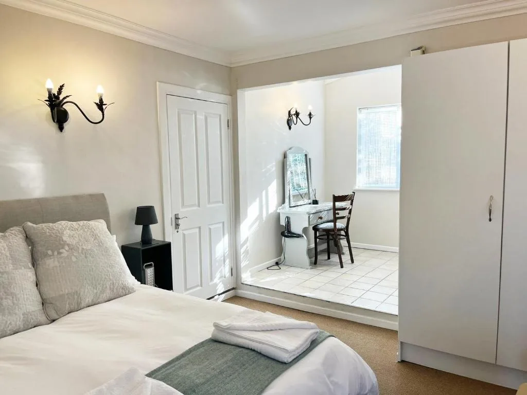 Bright bedroom with bed, wall sconces, and ensuite bathroom visible through open door