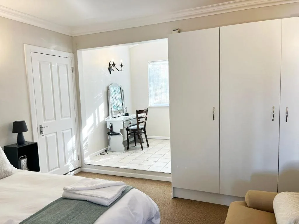 Bright bedroom with white bed, large mirrored wardrobe, and ensuite bathroom access