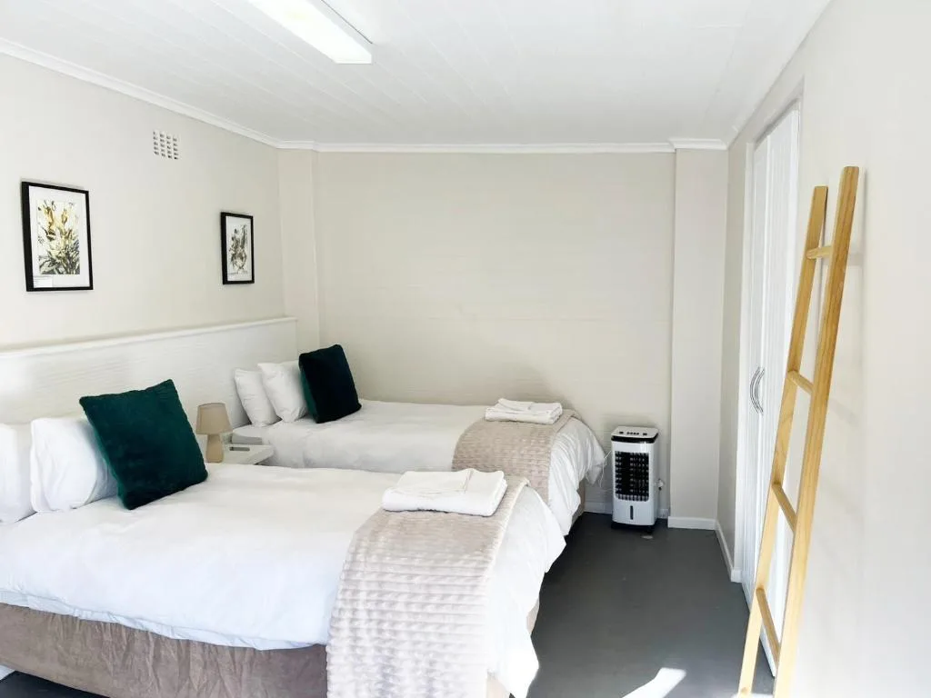 Bright bedroom with two twin beds, green pillows, framed botanical art