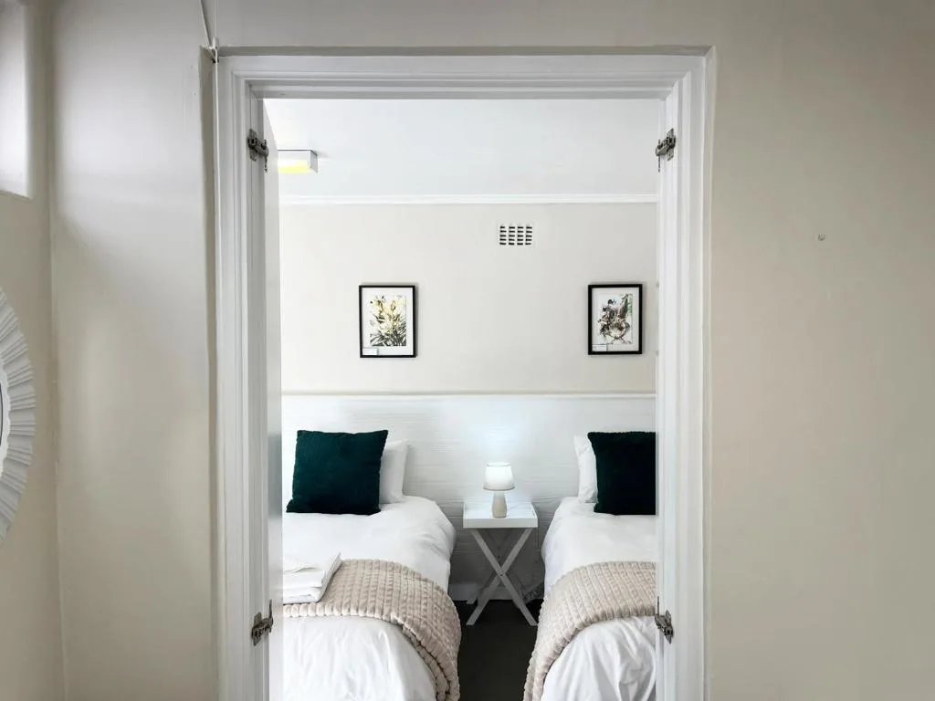 Twin beds with dark pillows, bedside table, botanical wall art and lamp