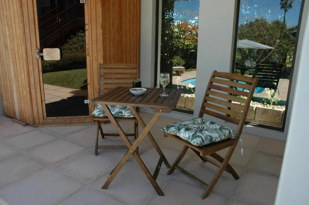 Wooden outdoor dining setup with chairs and table overlooking garden and pool