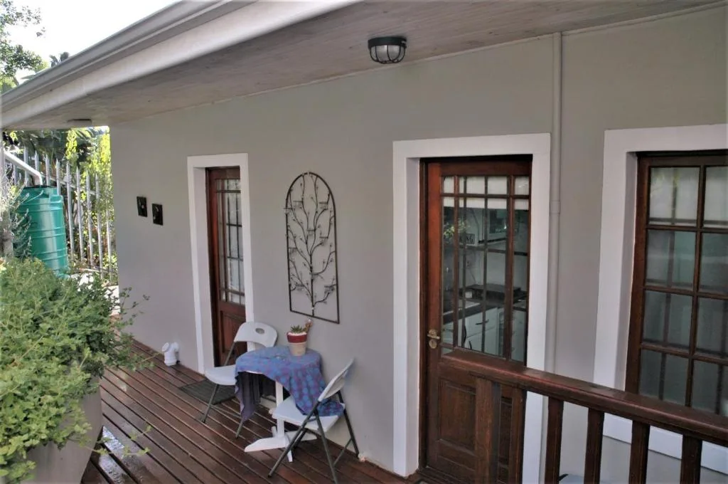 Covered wooden deck with white walls, dark wooden doors, and outdoor seating