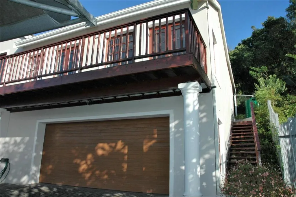 Modern white building with wooden deck and garage entrance under clear sky