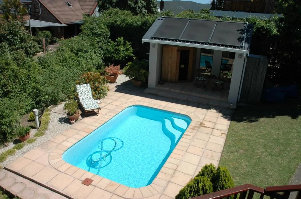 Bright blue swimming pool with terracotta deck and garden studio building