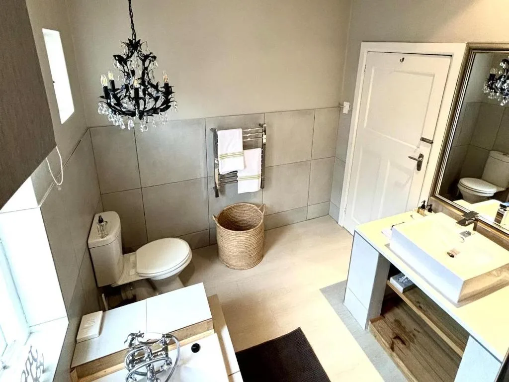 Modern bathroom with double vanity, toilet, soaking tub, and decorative chandelier