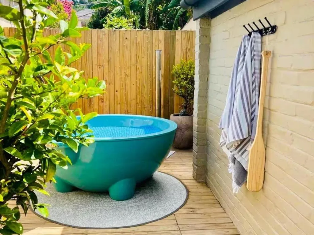 Turquoise soaking tub on wooden deck with garden and towel rack