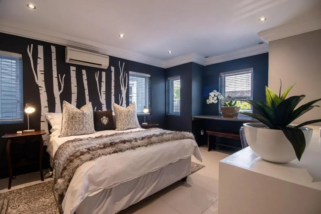 Modern bedroom with dark accent wall, white bedding, potted plant, and multiple windows