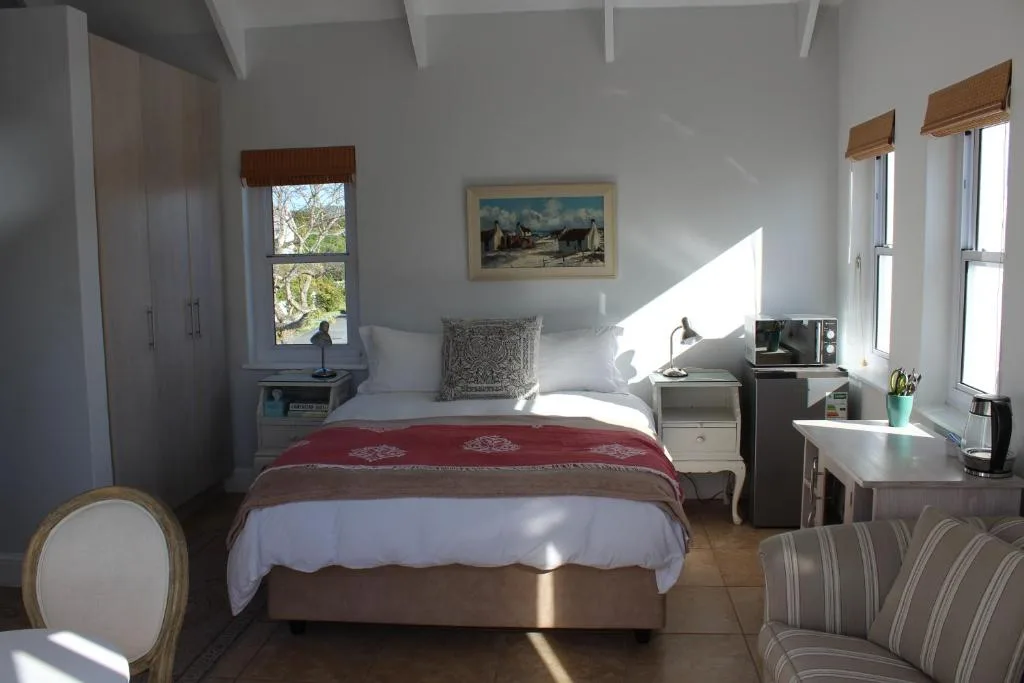Bright bedroom with red throw, white bedding, windows, and comfortable seating area