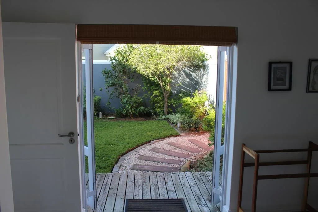 Wooden deck with open glass doors overlooking lush garden and pathways