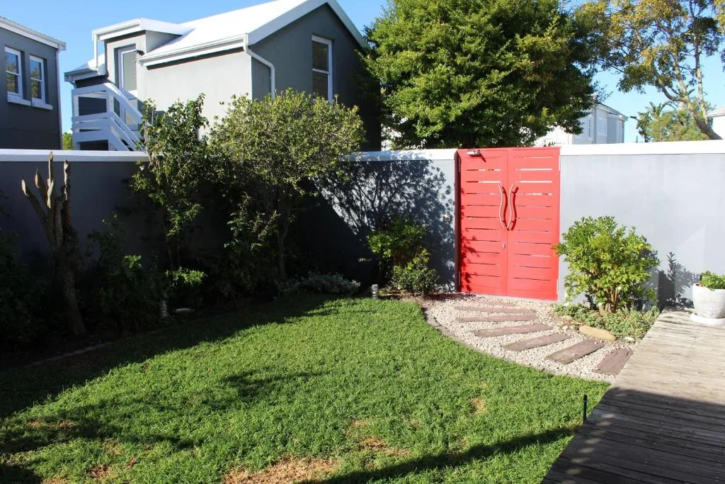 Modern home with manicured lawn, red gate, and surrounding gardens