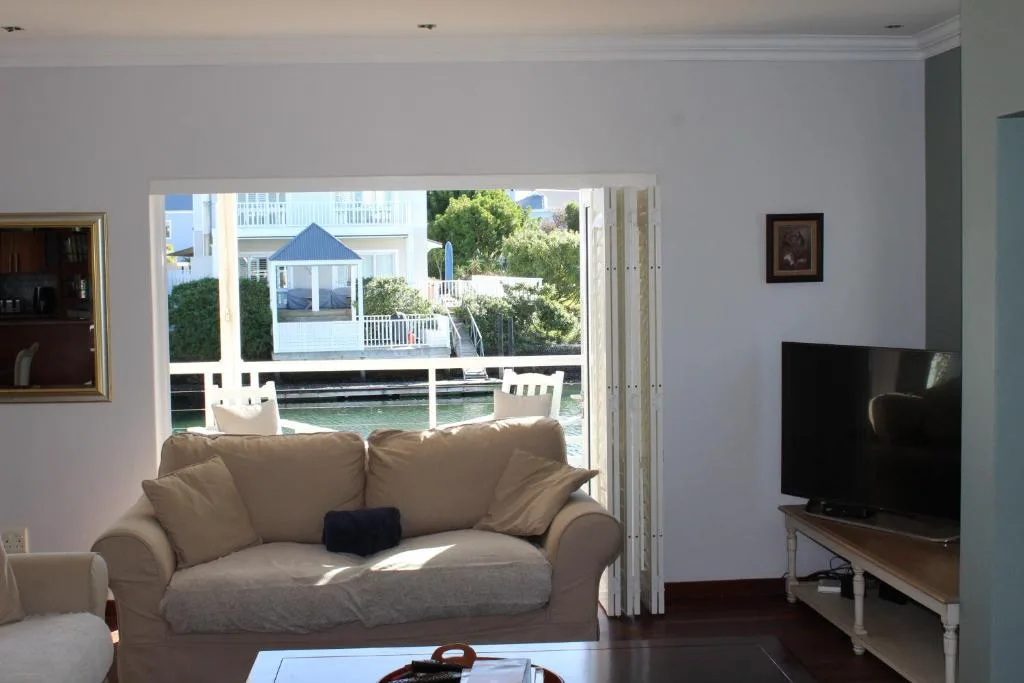 Bright living room with beige sofa, TV, and waterfront views through glass doors