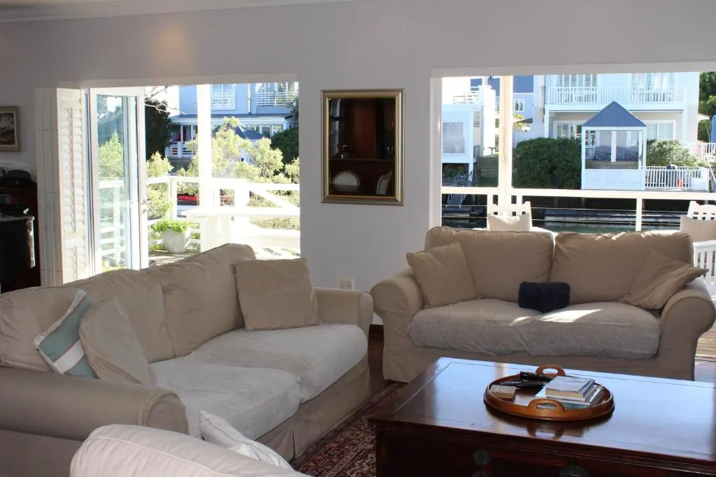 Bright living room with cream sofas overlooking garden and waterfront through large windows