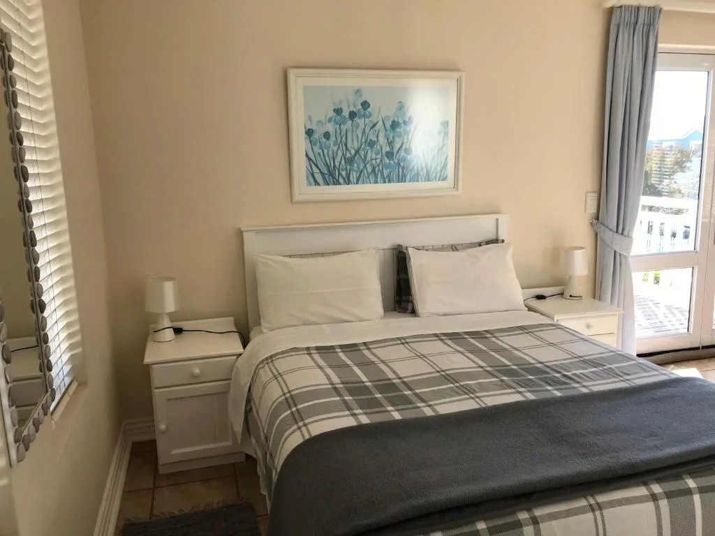 Bright bedroom with queen bed, floral artwork, and ocean view doors