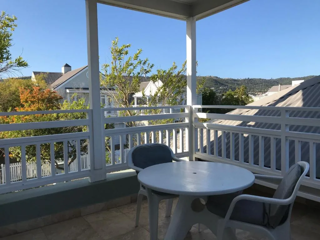 Covered deck with round table and chairs overlooking hillside gardens and homes
