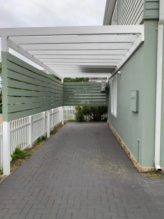 Covered outdoor patio with pergola, green privacy screening, and brick paving