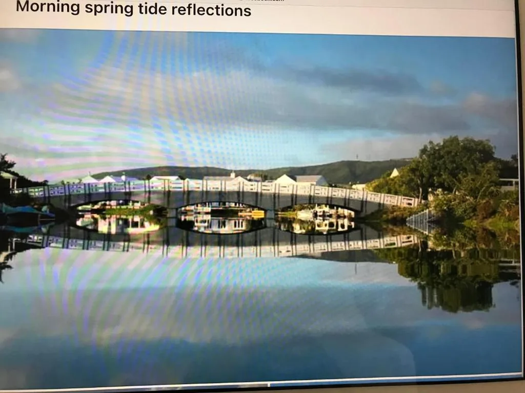 Serene morning lagoon reflections with waterfront buildings and mountains beyond