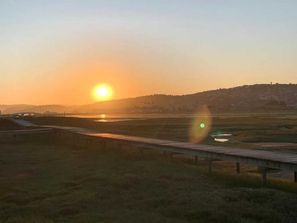 Golden sunset over Knysna Lagoon with hills and jetty visible