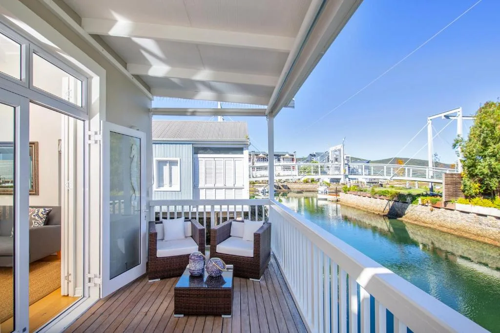 Covered waterfront deck with wicker seating overlooking Knysna lagoon and bridges