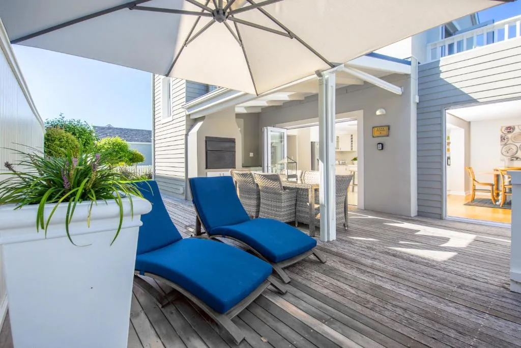 Covered deck with blue loungers, umbrella, and potted plants overlooking property
