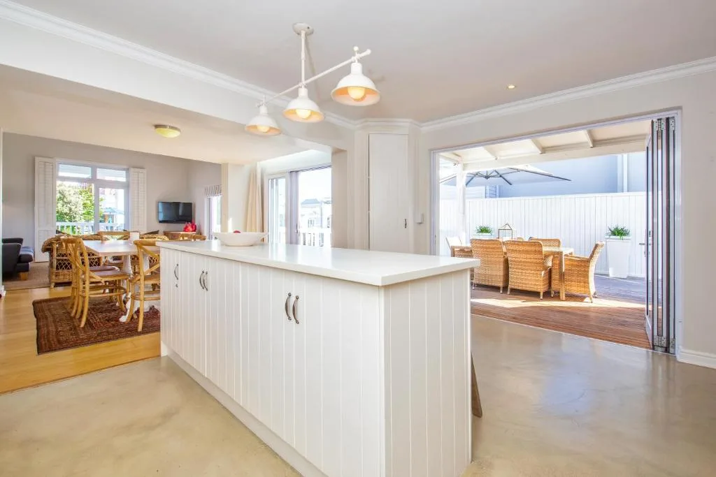 Modern white kitchen with island counter and pendant lights overlooking deck