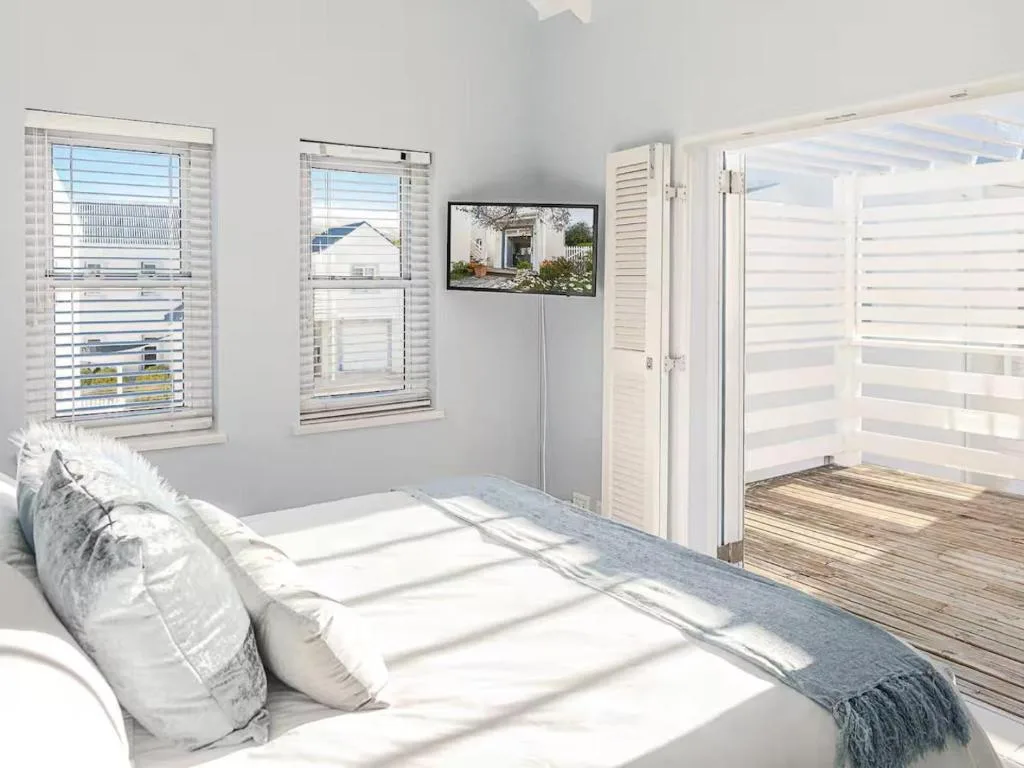 Bright bedroom with white bedding, coastal views through windows and glass doors