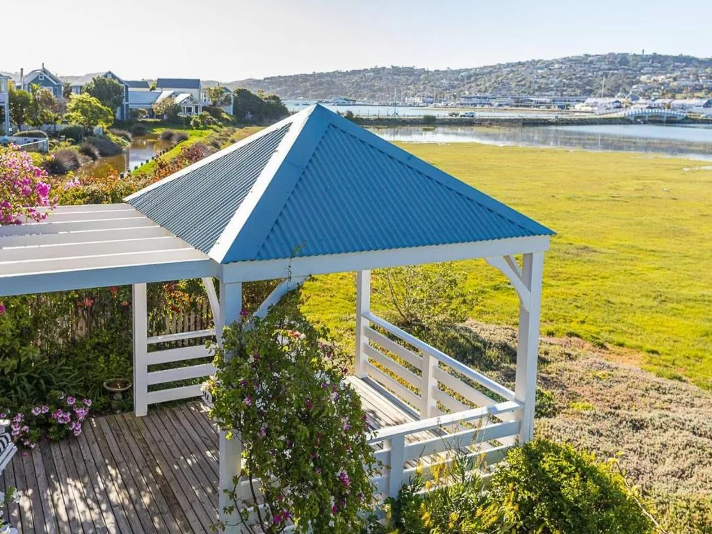 White wooden gazebo with blue roof overlooking lagoon and flowering gardens