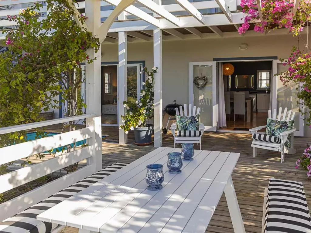 Spacious wooden deck with dining table, striped chairs, flowering bougainvillea, pergola