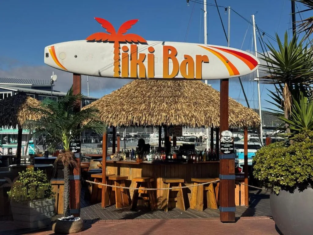 Colorful tiki bar with surfboard sign and thatched roof at marina