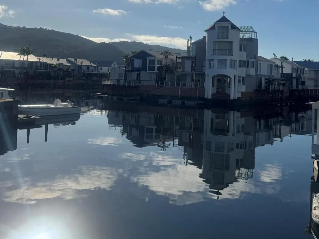 Waterfront properties reflected in calm lagoon water with mountains beyond
