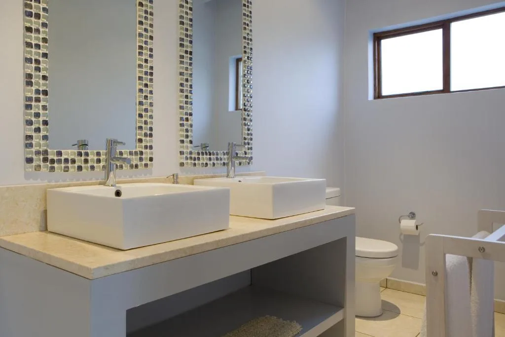 Modern bathroom with dual white vessel sinks, mosaic tile mirror, and window