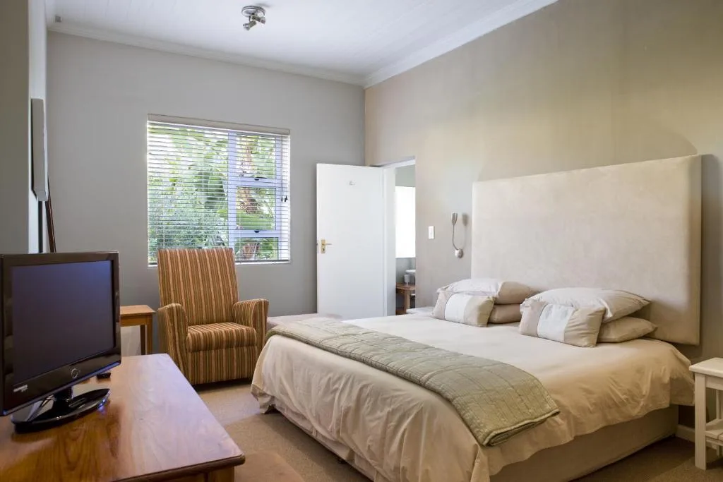 Spacious bedroom with queen bed, striped armchair, and garden views