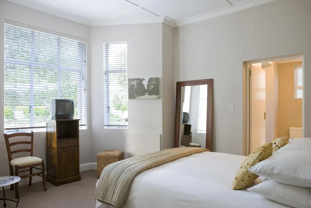 Bright bedroom with twin beds, wooden furniture, and garden views through shuttered windows