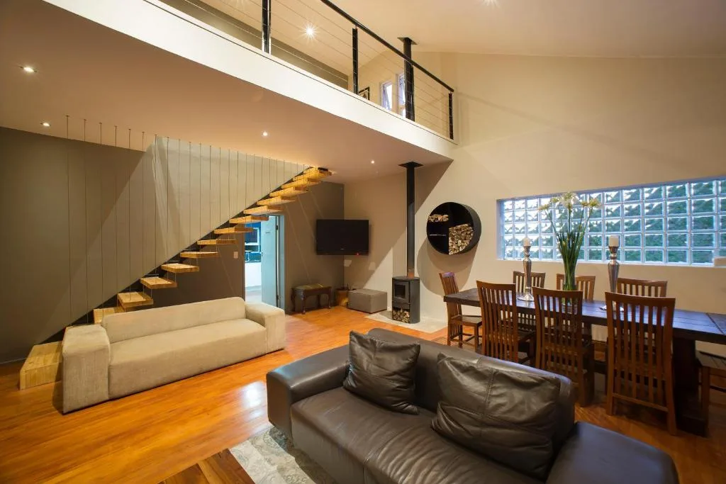 Modern open-plan lounge with leather sofa, staircase, and dining area beyond