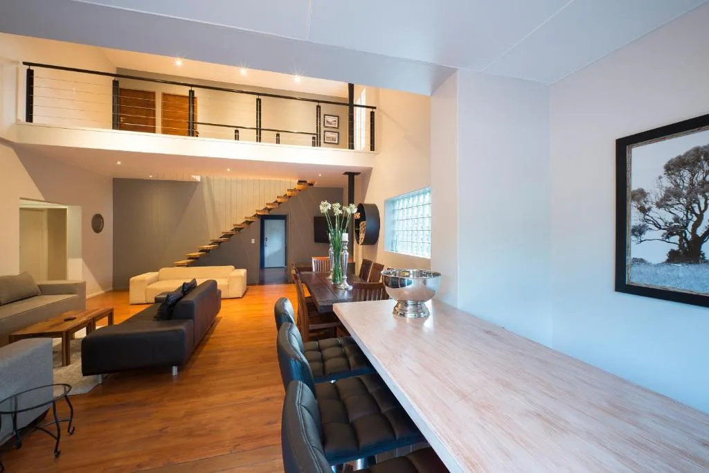 Open-plan lounge with black sofas, wooden floors, and mezzanine level above