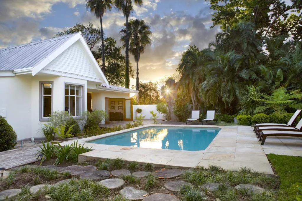 Sparkling swimming pool with lounge chairs and white manor house at sunset