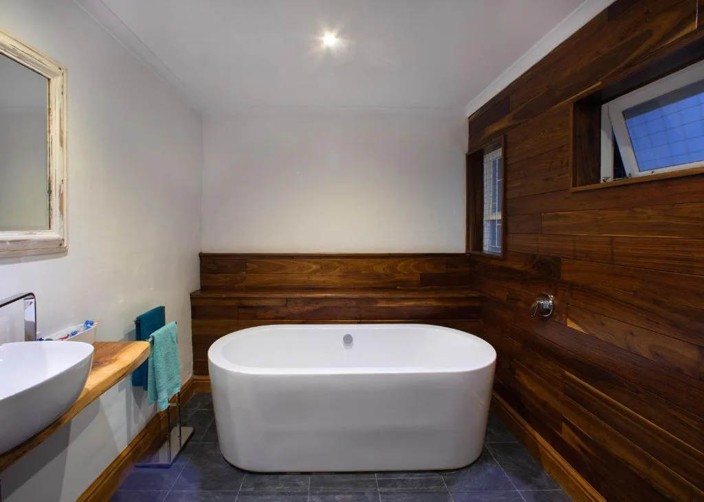 Modern freestanding bathtub with wooden paneling and vessel sink vanity