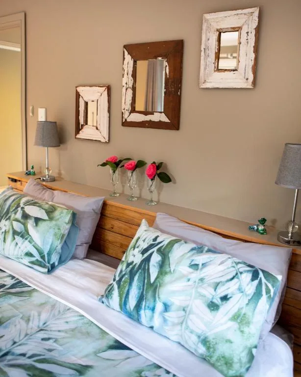 Bedroom with twin beds, botanical pillows, decorative mirrors, and fresh pink flowers