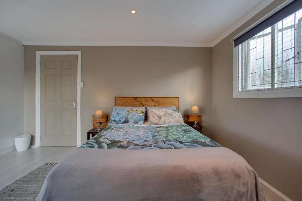 Bright bedroom with wooden bed frame, colorful bedding, and natural light from windows
