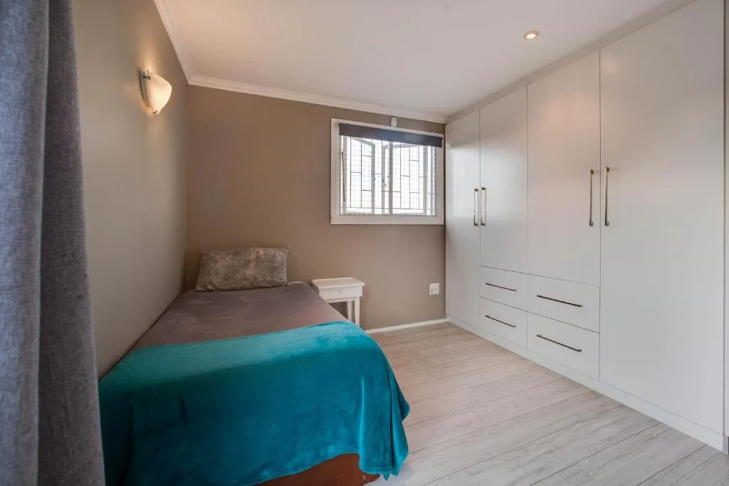 Bright bedroom with single bed, white built-in wardrobes, and window