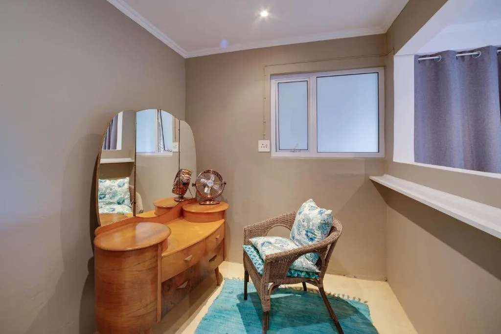 Bright bedroom with wooden dresser, mirror, and wicker chair by window