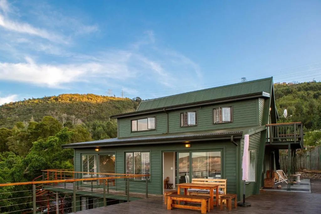 Green cottage with wooden deck and mountain backdrop