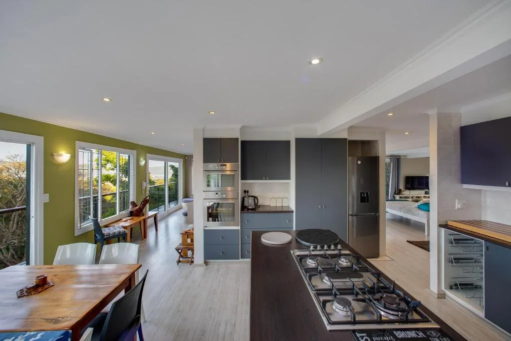 Modern open-plan kitchen with gas cooktop, dark cabinetry, and dining area beyond