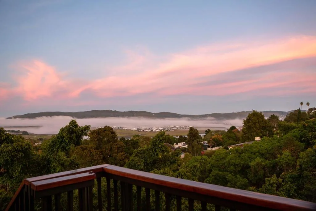Sunset over Knysna Lagoon with misty mountains and distant town lights
