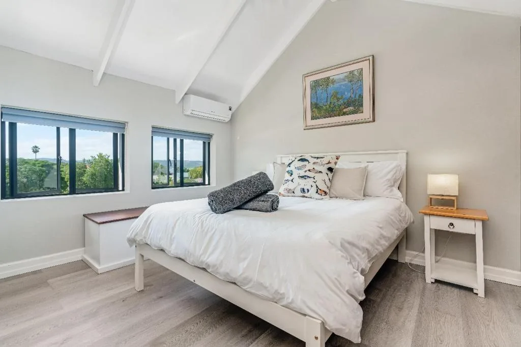 Bright bedroom with white bed, nightstand, and garden views through windows