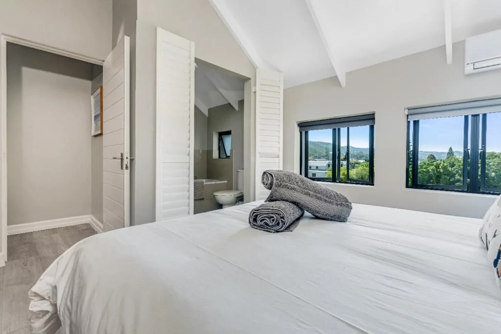 Bright bedroom with white bed, folded towels, and scenic mountain views through windows